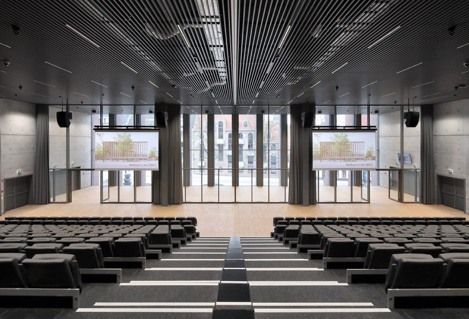 The BMCC auditorium: rows of seats facing two screens and a glass wall onto the square.
