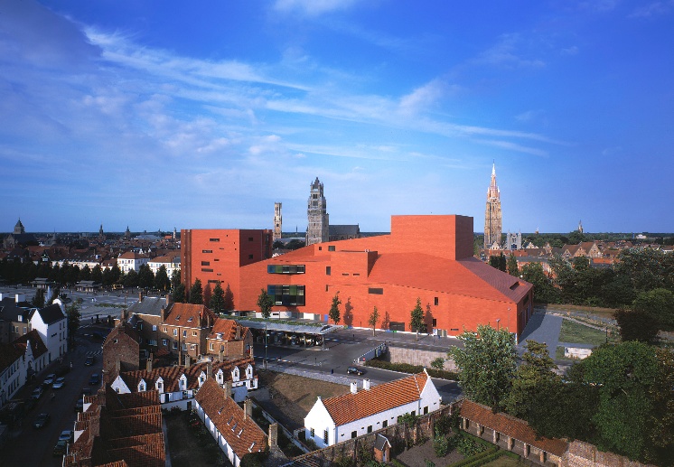 Concertgebouw Brugge seen from above: red brick volumes at the edge of the old city, with the towers of Bruges behind.