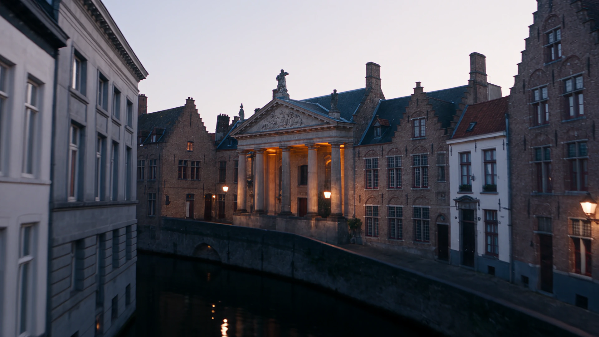 Bruges at dusk, lamplight on a civic frontage above a still canal.